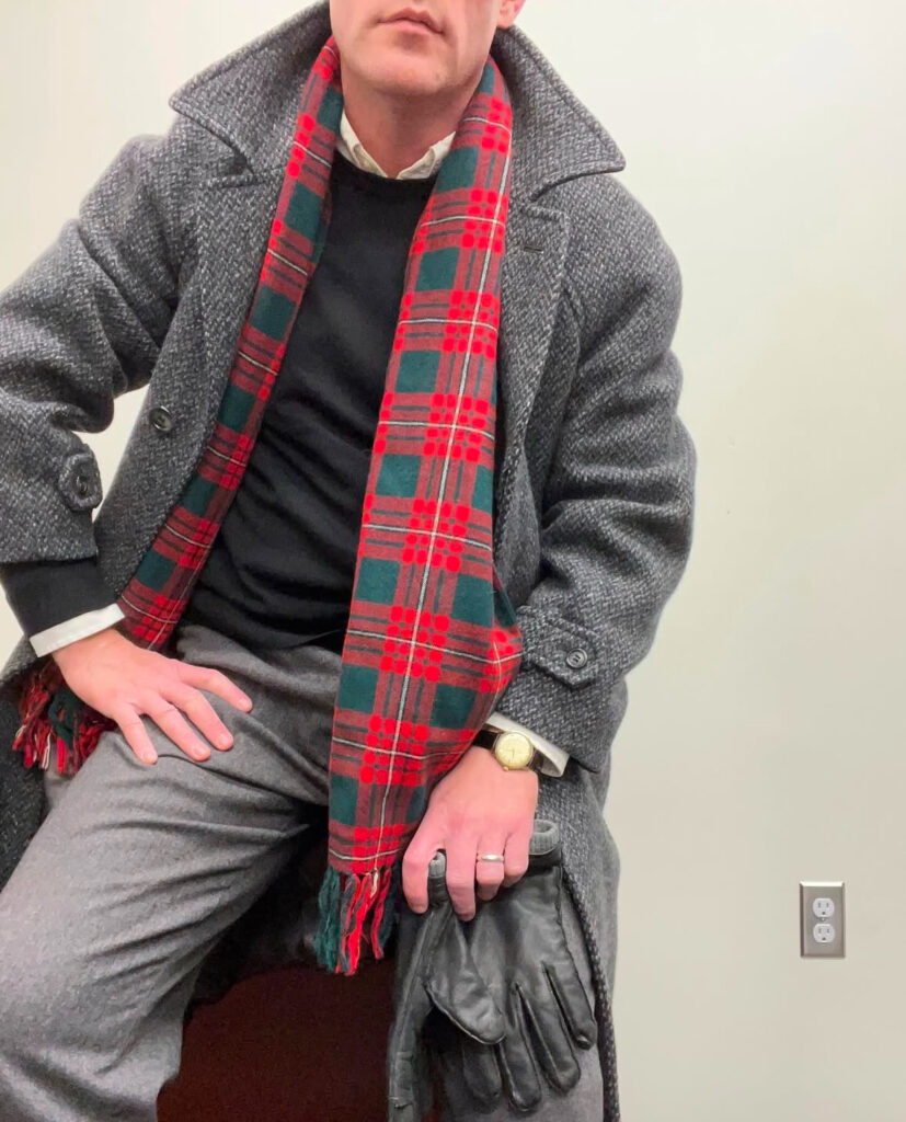 A man wearing an excellent balmacaan, tartan scarf, and wristwatch