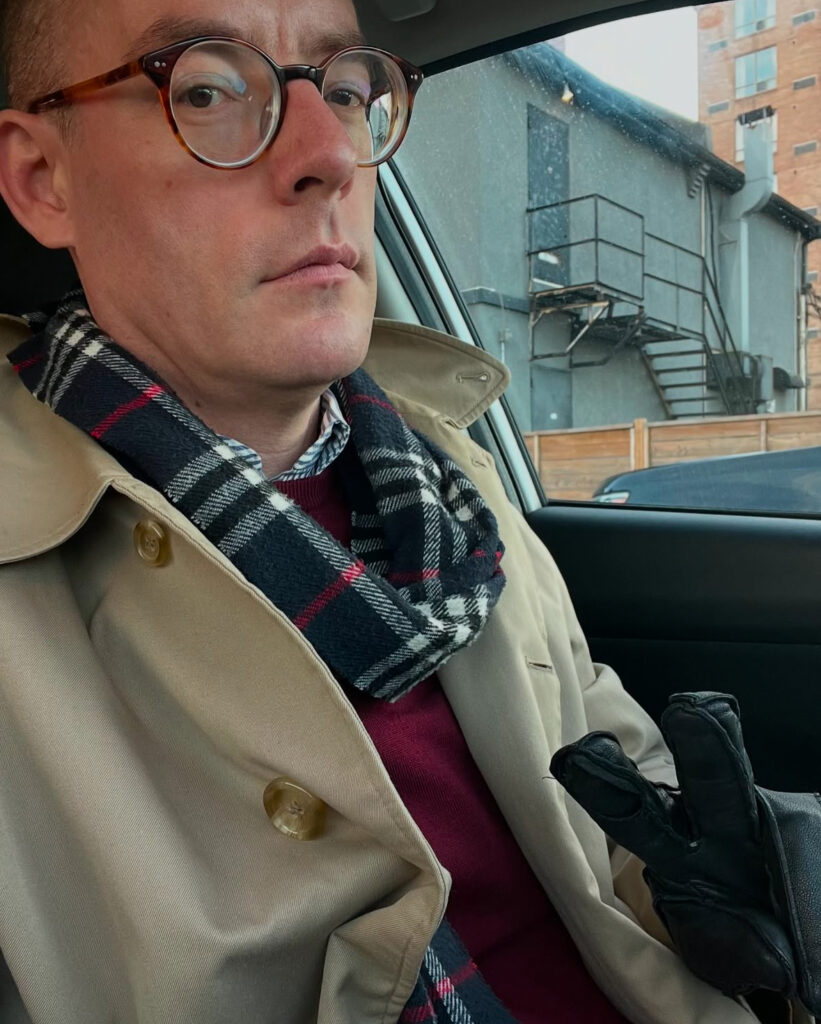 a car selfie of a sober, well-dressed man giving a peace sign with gloved fingers