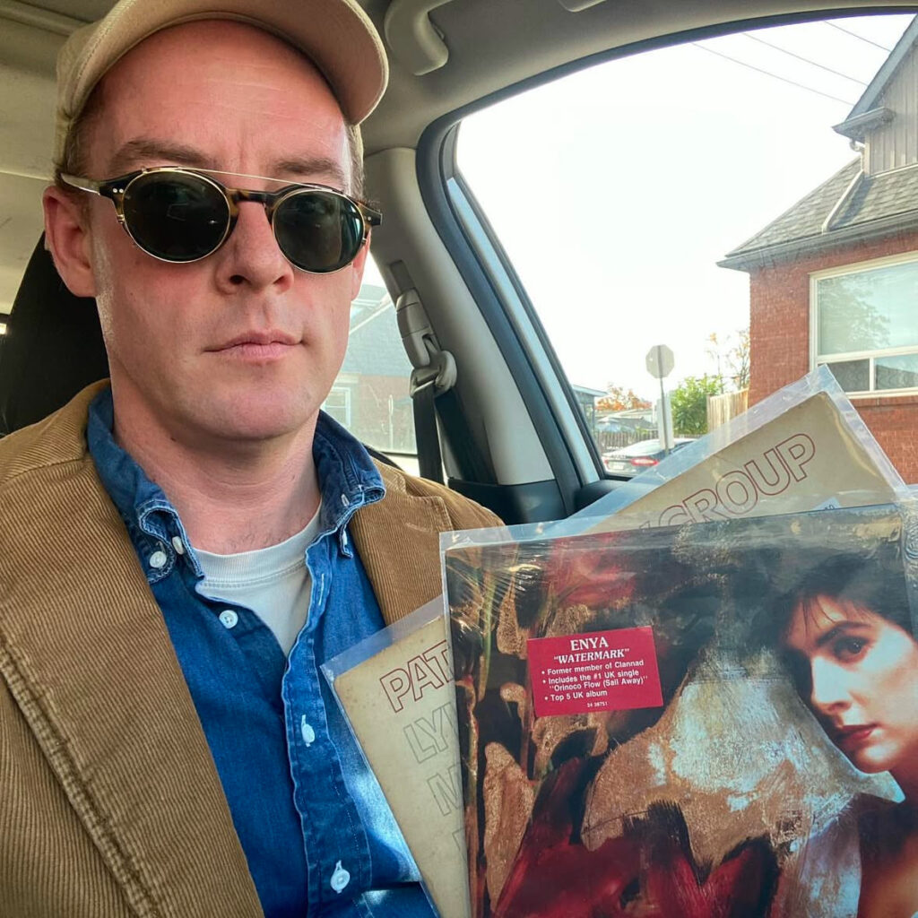 A man in sunglasses and a corduroy cap holding an Enya album