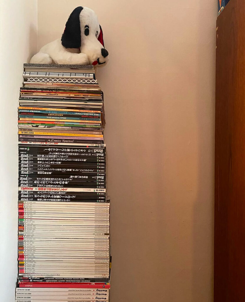 a stuffed white dog sitting atop a stack of magazines at least waist height