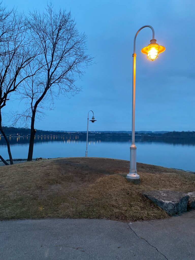 An evening looking out over a lake with a warm streetlamp in the foreground